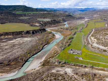 Aerial view of a river winding through a green meadow and past ancient ruins in the valley,