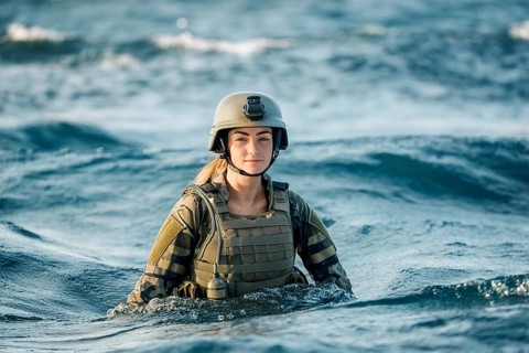 Soldier in uniform and helmet stands up to his chest in the sea, surrounded by waves, AI generated,