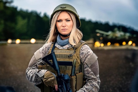 Woman in military uniform and helmet holding a gun in front of a tank on a forest road, AI
