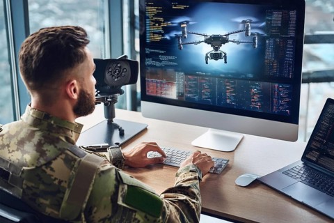 A soldier works in front of a large screen showing technical details and programming of a drone, AI