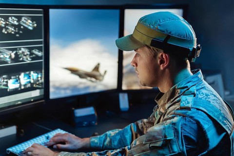 A soldier concentrates on watching aircraft simulations on large monitors in the control room, AI