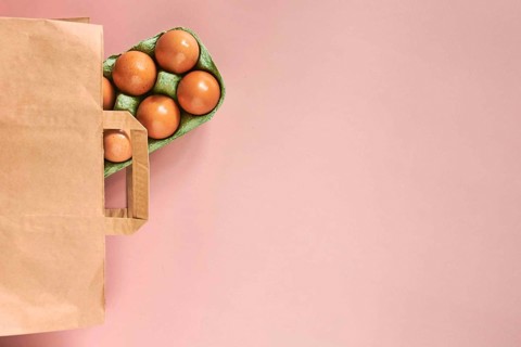 Kraft bag with chicken eggs in tray on beige background, shopping concept, space for text