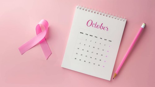 Top view of October calendar and a breast cancer awareness pink ribbon over a pastel pink