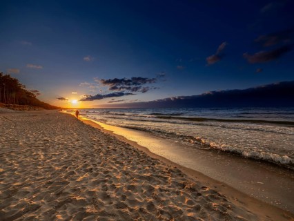 A man walks at sunset on the sandy beach on the island of Usedom on the Baltic Sea, Zempin,