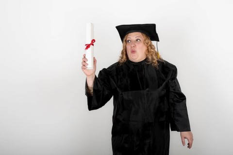 Recent graduate woman, dressed in cap and gown, showing off his degree