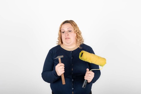 Woman looking confused at a paint roller and hammer