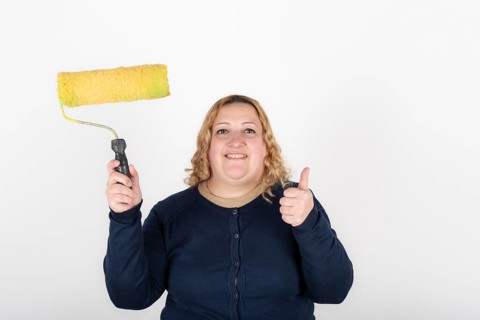 Smiling woman holding a paint roller and giving thumbs up