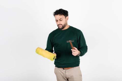 Man looking confused at a paint roller and hammer