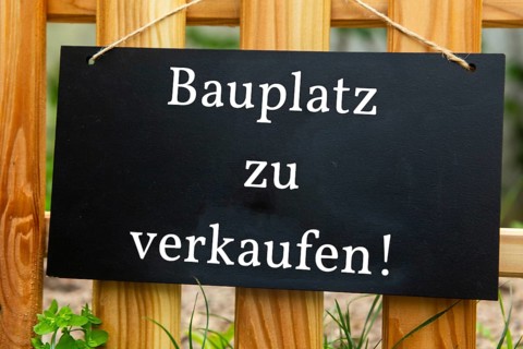 Sign with the inscription BAUPLATZ ZU VERKAUFEN on a wooden fence (symbolic image)