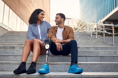 Couple, man with prosthetic leg, sitting on the steps in the city, the woman laughs at her partner