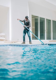 Home pool cleaning with wall brush. Male worker cleaning a home swimming pool with special brush