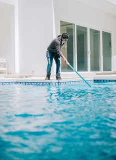 Young man cleaning a swimming pool with suction hose. Swimming pool cleaning and maintenance