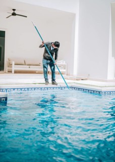 Worker cleaning a beautiful homemade swimming pool with skimmer. Maintenance person cleaning a