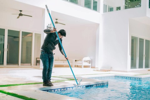 Person cleaning swimming pool with special brush. Maintenance person cleaning home pool with broom