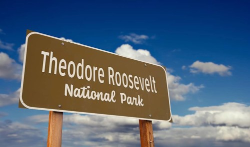 Theodore roosevelt national park (north dakota) road sign against blue sky and clouds