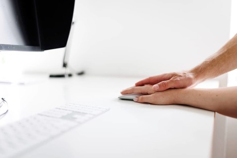 Topic: sexual assault in the workplace. A man's hand rests on a woman's hand at a desk. Berlin, 25
