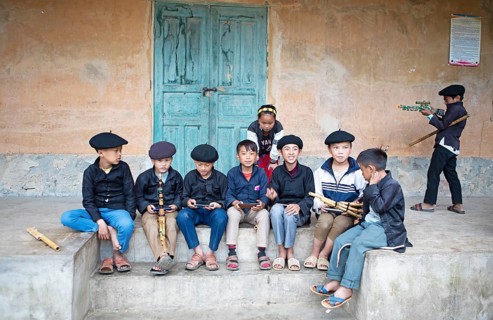 Vietnamese boys in traditional clothes and with traditional flutes playing with their mobile