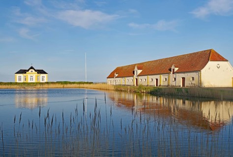 Building and house by the lake with reflection in the calm water under a blue sky, Valdemars Slot,