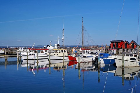 Boats in the harbour are reflected in the calm water under a bright blue sky, Herrenhausroute,