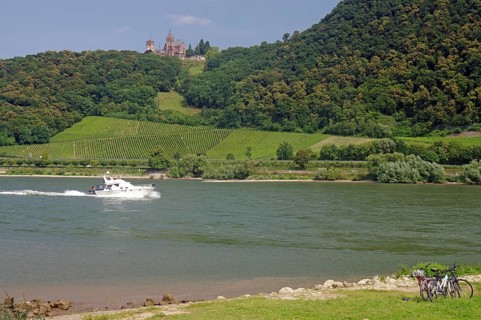A motorboat sailing on a river surrounded by vineyards and a castle on the hill, cycle tourism,