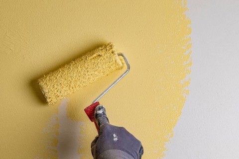 Wall is painted with yellow paint, hand with paint roller