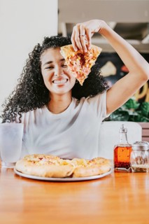 Smiling afro woman enjoying a pizza in a restaurant. Happy afro hair woman showing slice of pizza