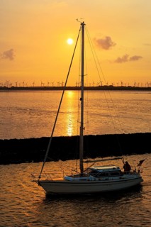 Sailboat on the North Sea at sunrise in front of mudflats and wind turbines, Norddeich, East