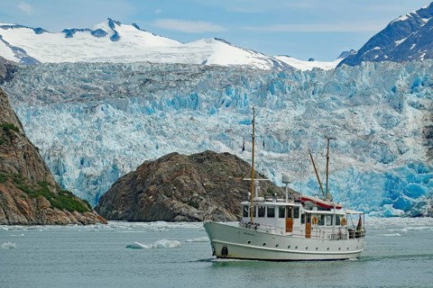 Small boat in front of the ice front of a glacier calving into the sea, Tracy Arm Fiord, Climate