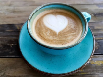 A blue ceramic cup with a heart made of milk foam on a wooden table embodies cosiness