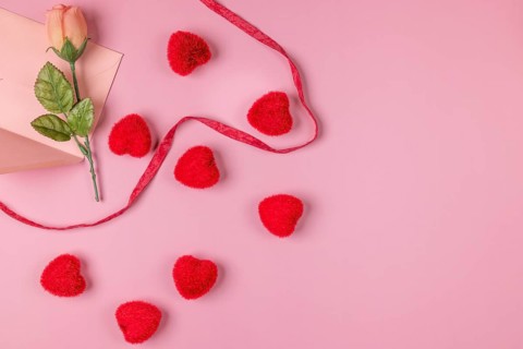 Romantic Valentine's Day scene with rose, envelope and red hearts on a pink surface