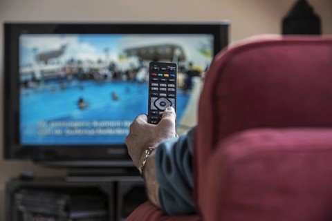 Man in comfy chair switching channels with remote control to look for pleasing programme on