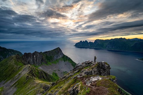 Hiker standing on summit, fjord and mountains, mountain range Okshornan in the back, Senja, Norway,