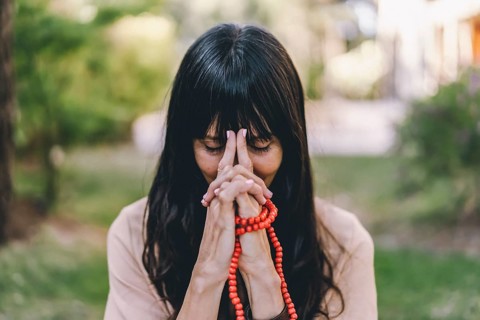 Woman practicing meditation sitting in yoga asana Kali Mudra holding a japa mala outdoors