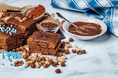 Brownies filled with jam surrounded by ingredients for decoration, chocolate icing, mixed nuts,