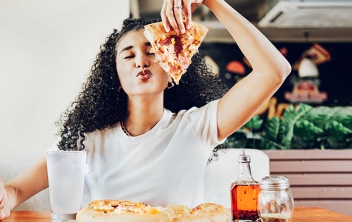Girl in a restaurant showing slice of pizza giving a kiss to the camera. Beautiful curly haired