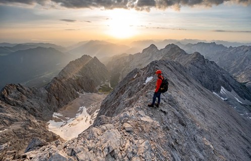 Mountaineer with helmet on a narrow mountain ridge at sunrise, crossing the JubilÃ¤umsgrat, view of