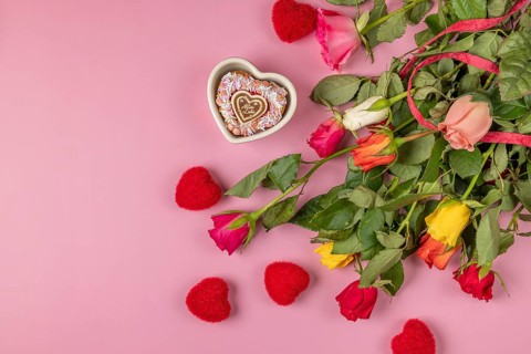 Colourful bouquet of roses with red hearts and heart-shaped bowl with muffin on a pink background