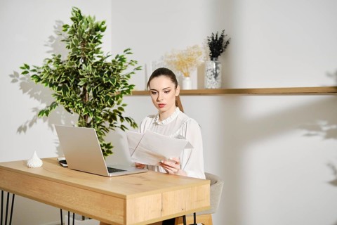 Woman checking tax return sitting in bright office at a desk with laptop
