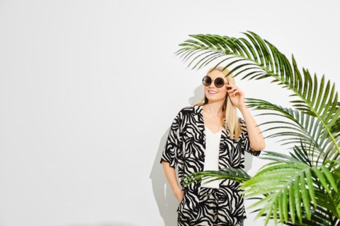Happy woman stands by vibrant green palm leaves, creating a sense of mystery and connection with