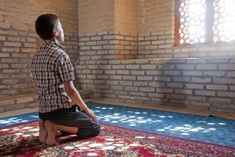 Praying Turkmen boy sitting on his knees in front of window in old Mosque in the ancient city of