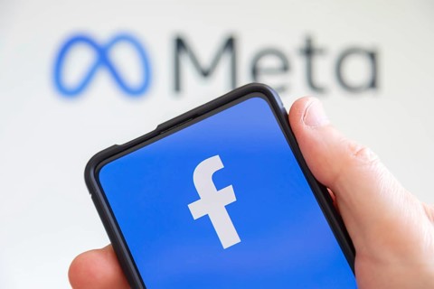 Hand holding mobile phone with Facebook and Meta logo social media computer screen