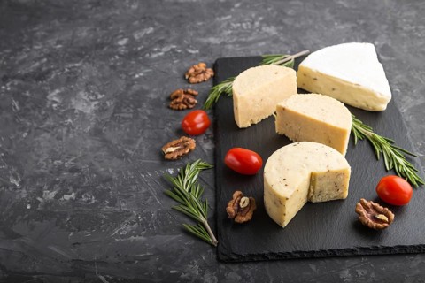 Cheddar cheese and various types of cheese with rosemary and tomatoes on black slate board on a