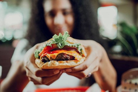 Close-up of a girl showing appetizing hamburger in a restaurant. Hands of girl showing burger in a