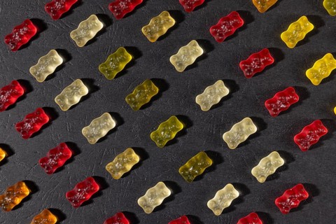 Different coloured gummy bears in rows, on a dark background