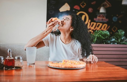 Lifestyle of afro-haired woman enjoying a pizza in a restaurant. Happy afro hair woman eating pizza