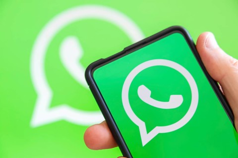 Hand holding mobile phone with WhatsApp logo messenger app computer screen