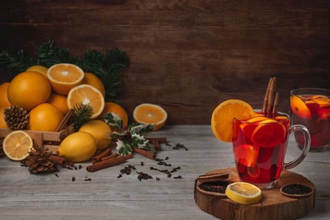 Wooden basket with oranges and lemons, two glass cups with punch, cloves and cinnamon sticks,