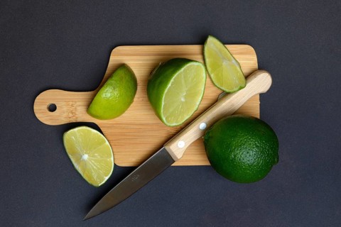 Halved limes on a chopping board with a kitchen knife