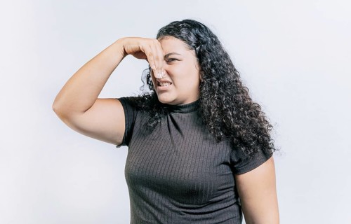 Young woman covering her nose from a bad smell isolated. Displeased girl holding her nose isolated.