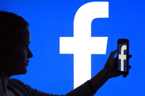 Silhouette of a woman with a smartphone in her hand in front of a Facebook logo, 12/01/2016